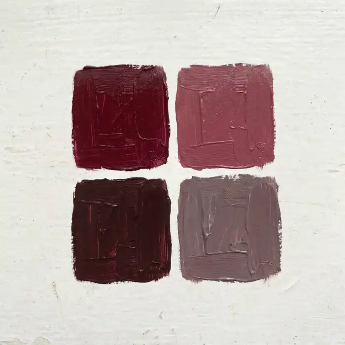 Four small, hand-painted color swatch chips in varying shades of deep red, arranged in a grid on a pale background, photographed from directly above.
